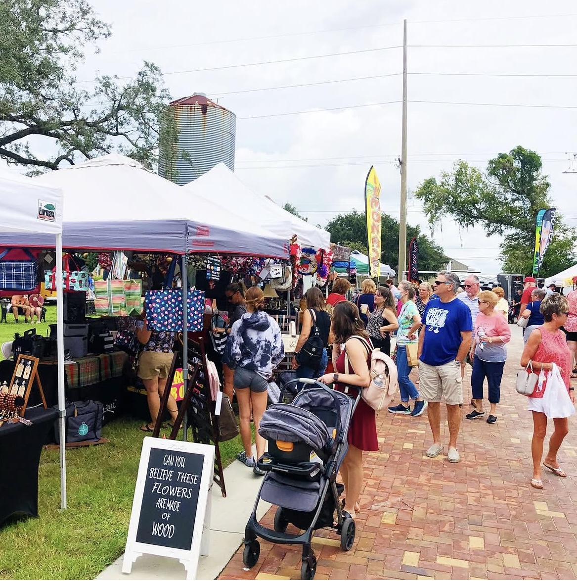 Vendors and shoppers at the Winthrop Pop Up Market — handmade goods, art, and a chalkboard sign reading 'Can you believe these flowers are made of wood.'